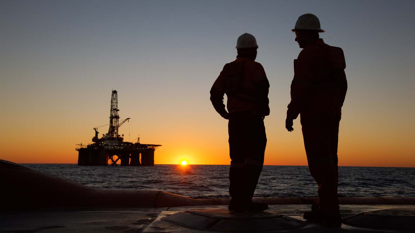 Two workers looking at oil rig on sunset horizon